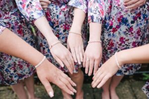 Five hands of bridesmaids dressed in flowery dresses, showcasing elegant and coordinated style.