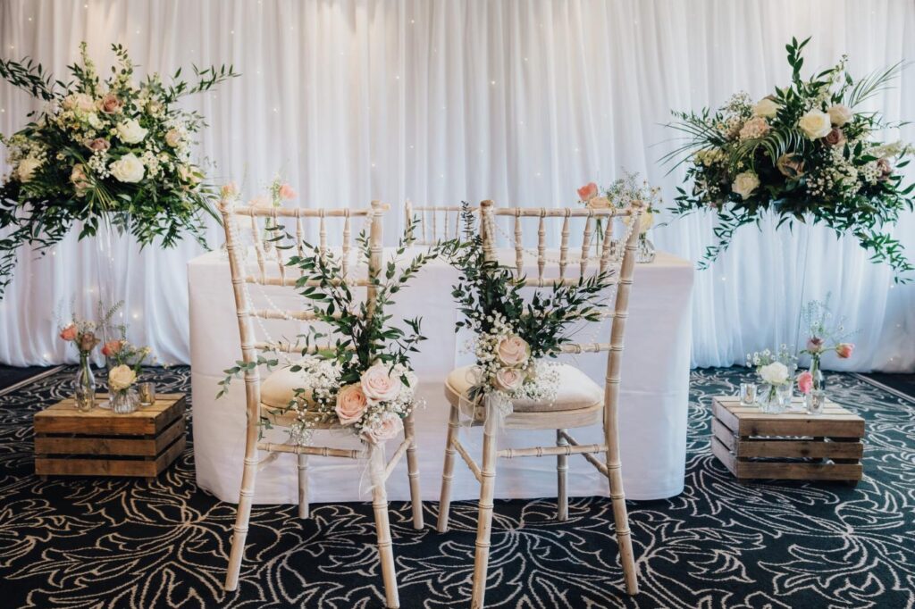 Two white cream wedding chairs adorned with delicate floral arrangements.